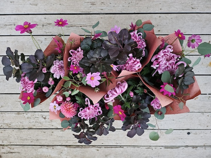 Farmer market bouquets wrapped in brown craft paper and arranged together including cosmos, mums, and a dark purple smokebush foliage.